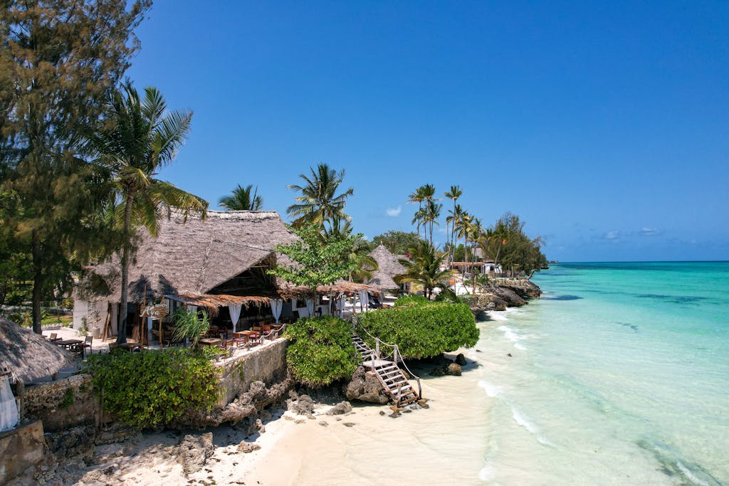 Beautiful tropical beach resort in Zanzibar, Tanzania, with thatched huts, palm trees, and turquoise waters.