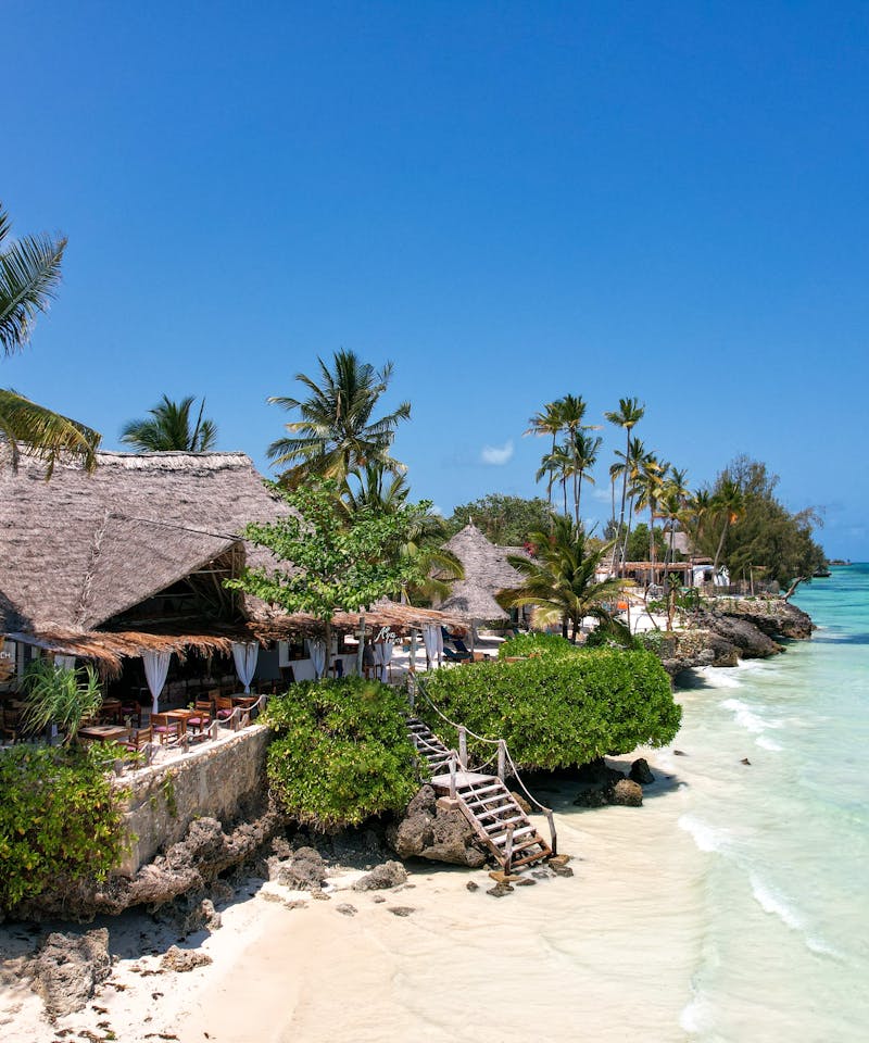 Beautiful tropical beach resort in Zanzibar, Tanzania, with thatched huts, palm trees, and turquoise waters.