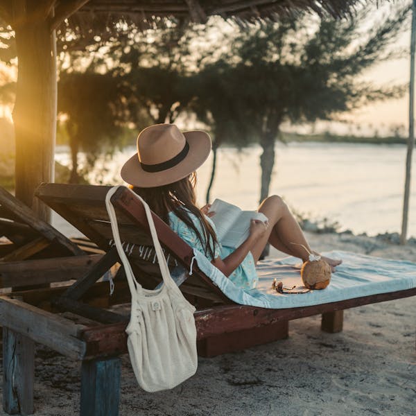 Woman reading on a beach lounger under a sun hat in Zanzibar at sunset, embracing vacation tranquility.